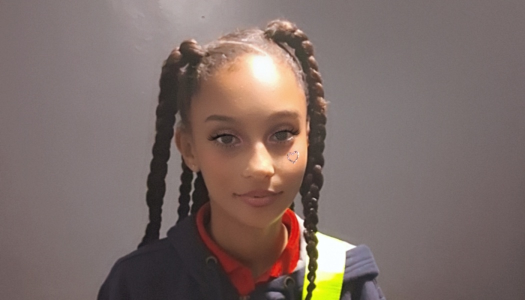 Young girl with long braided pigtails, a small heart under her eye, wearing a high-visibility vest.
