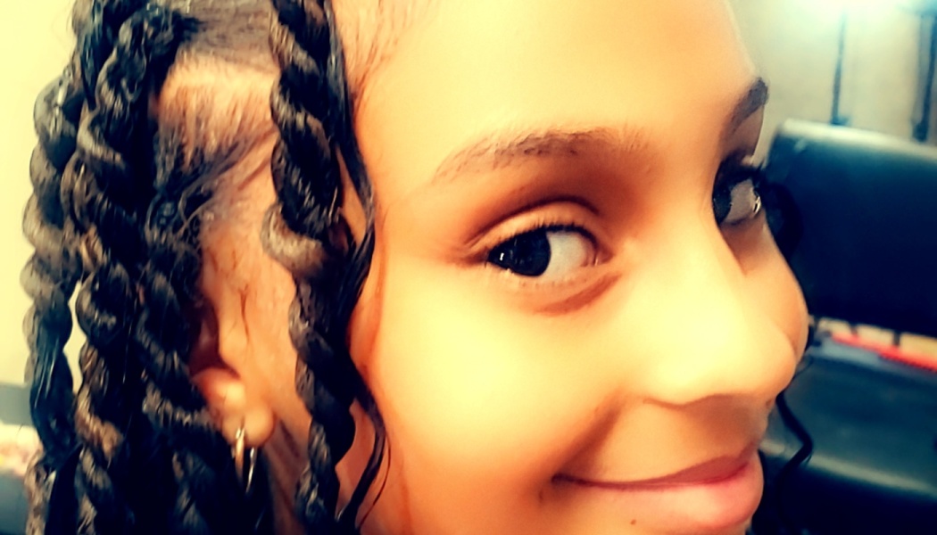 Close-up of a smiling young girl with dark twisted braids framing her face.