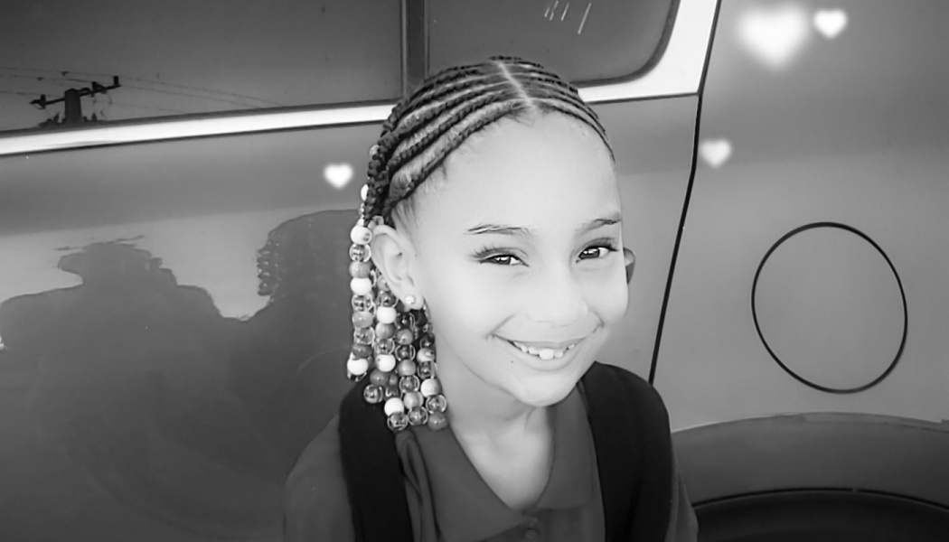 A smiling young girl with cornrow braids and decorative beads in a black-and-white portrait.