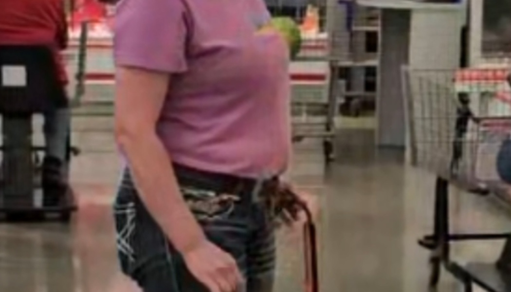 A woman in a purple t-shirt and jeans standing in a store with a small green bird peeking out of her shirt.