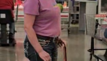A woman in a purple t-shirt and jeans standing in a store with a small green bird peeking out of her shirt.