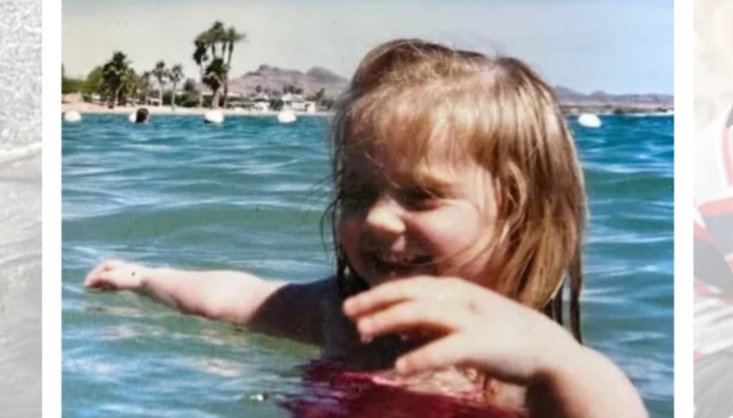 A smiling young girl playing in blue water with her arms outstretched and palm trees in the background.