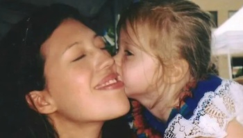 A young blonde girl kisses a smiling dark-haired woman on the cheek.