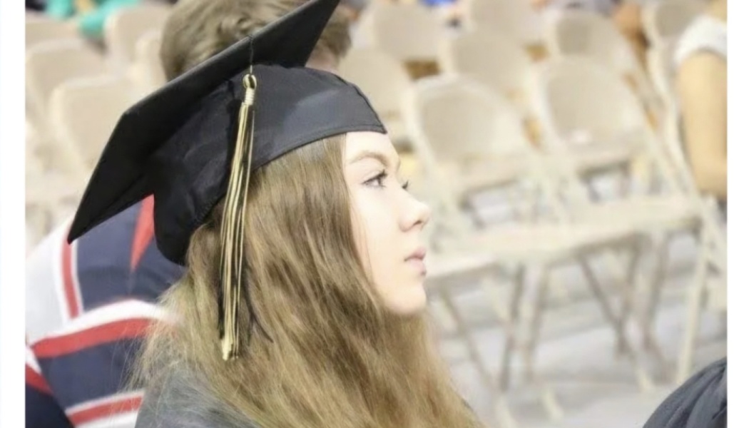 Young woman with long hair wearing a black graduation cap and tassel looking forward at a graduation ceremony.
