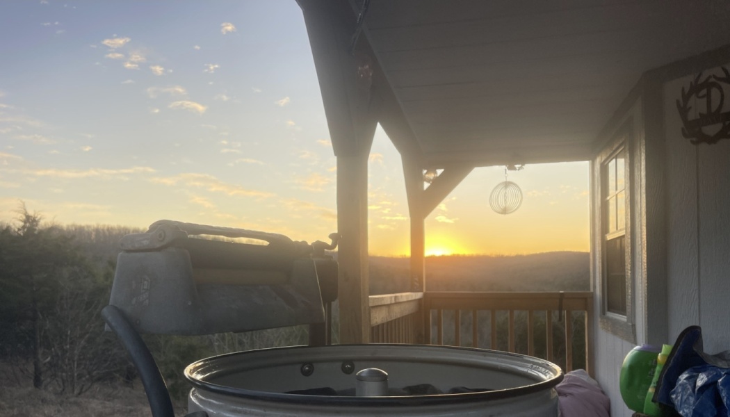 Vintage wringer washing machine on a wooden porch overlooking a golden sunset over rolling hills.