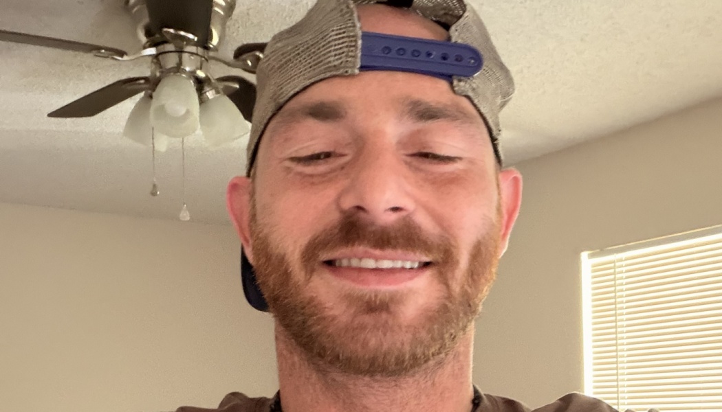 Smiling bearded man wearing a backward mesh trucker hat indoors.