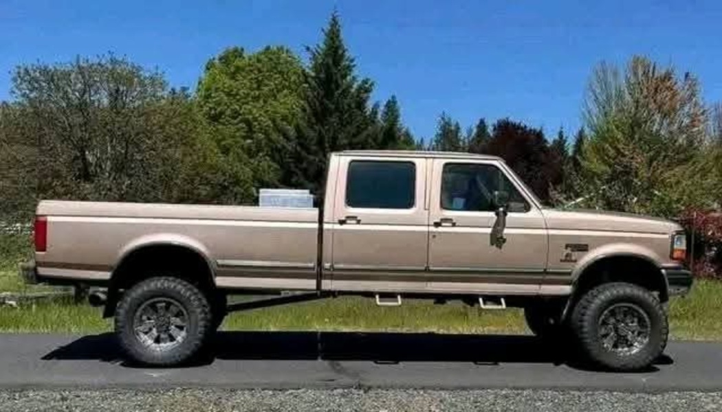 Side view of a vintage tan Ford crew cab pickup truck with lifted suspension and off-road tires.