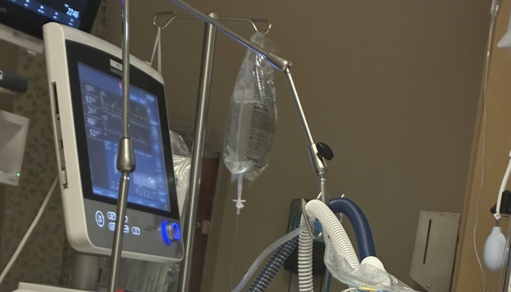 Hospital ventilator monitor displaying medical data next to an IV drip bag and breathing tubes.