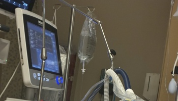 Hospital ventilator monitor displaying medical data next to an IV drip bag and breathing tubes.