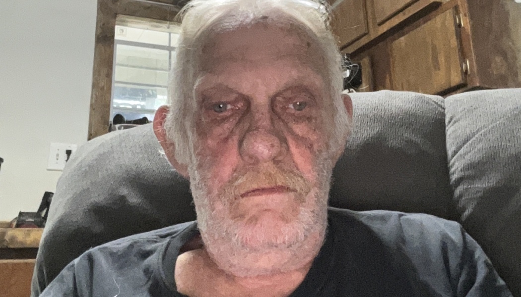 An elderly man with white hair and a gray beard sitting in an armchair, looking directly at the camera.
