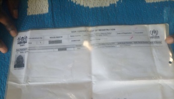 Hands holding a GOK and UNHCR Proof of Registration document displaying refugee details and an ID photo.