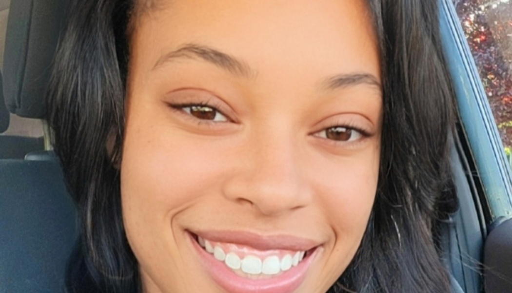 Close-up portrait of a young Black woman with dark hair smiling warmly inside a car.