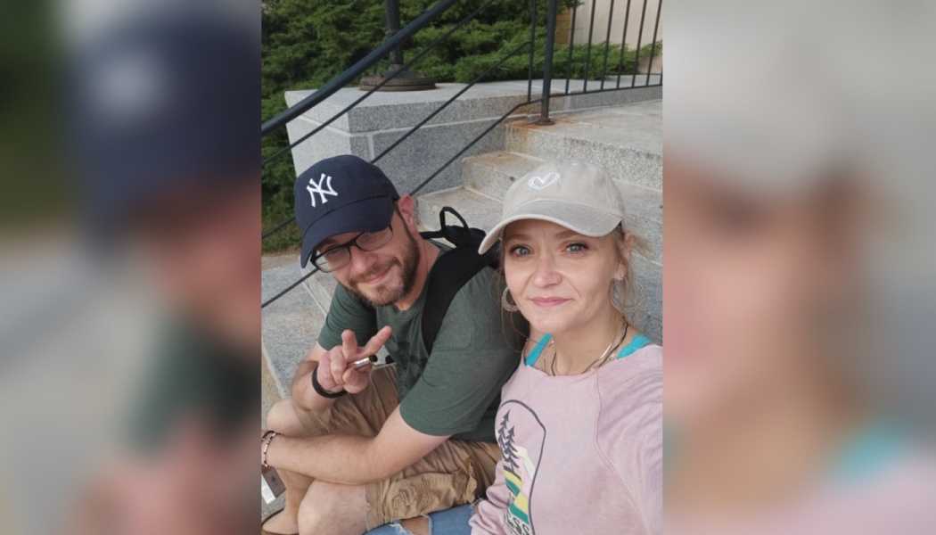 A smiling couple wearing baseball caps sitting together on outdoor stone steps.
