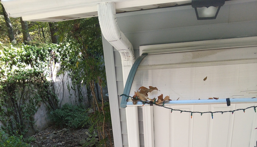 A white door awning decorated with string lights and dry leaves next to a white gutter downspout.