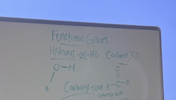 Handwritten chemistry notes about functional groups on a whiteboard outdoors against a blue sky.