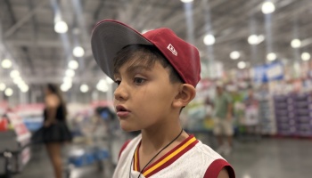 Young boy wearing a red baseball cap and sports jersey looking thoughtfully off-camera in a store.