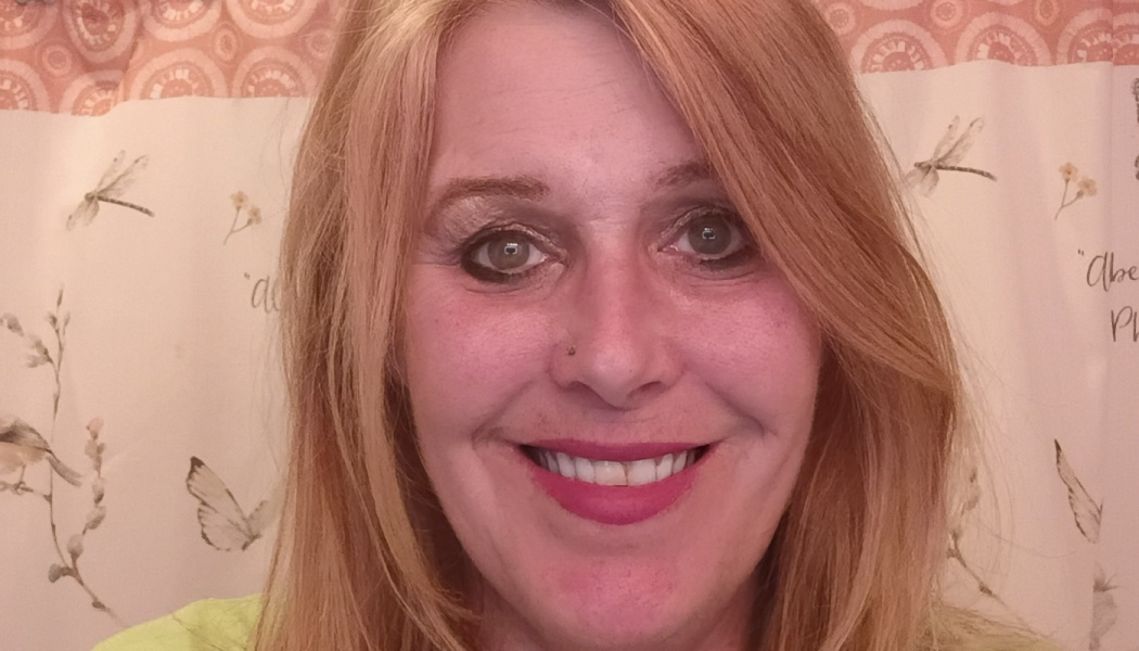 Close-up portrait of a smiling woman with strawberry blonde hair and bright pink lipstick.