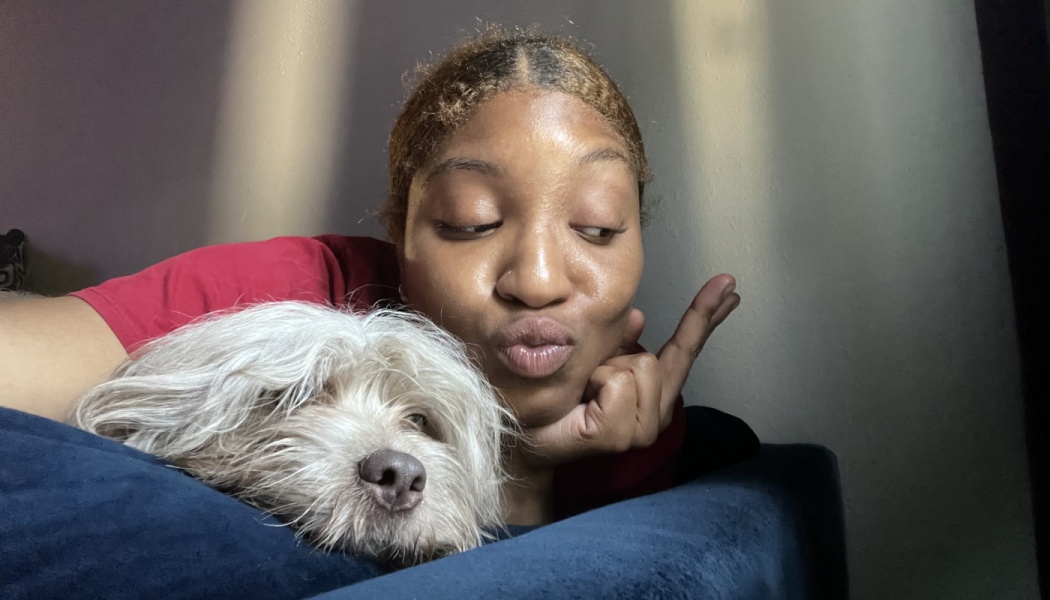 A woman making a kissy face lying beside a small, fluffy white dog resting on a blue couch.