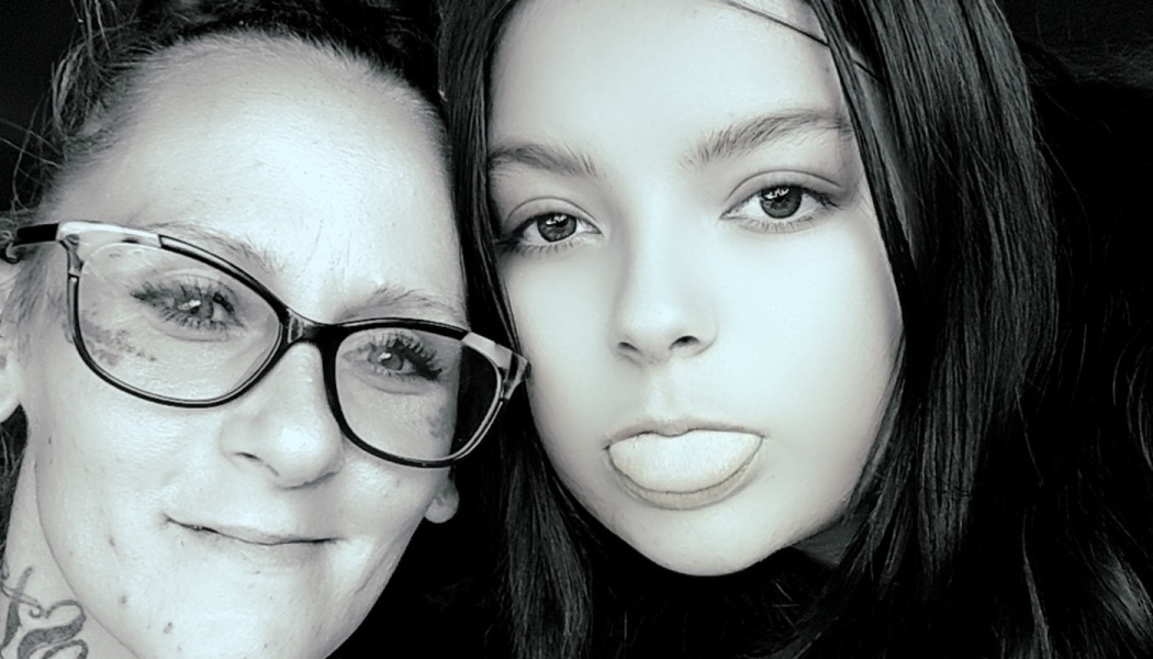Black-and-white close-up of a smiling woman with glasses next to a young girl playfully sticking her tongue out.