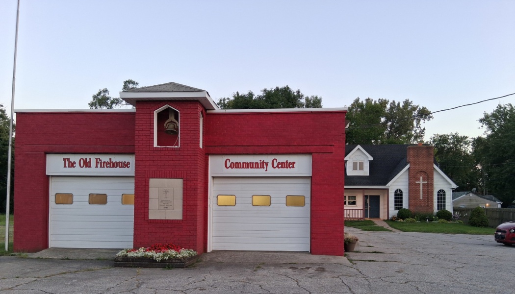 Exterior of The Old Firehouse Community Center, a red brick building with white garage doors and a bell tower.
