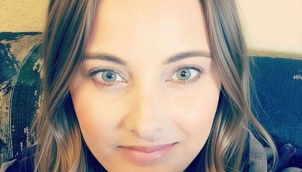 Close-up portrait of a woman with light wavy hair and bright green eyes looking at the camera with a gentle smile.