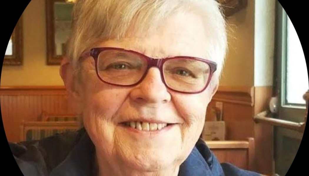 Close-up of a smiling senior woman with short white hair and red-rimmed glasses.