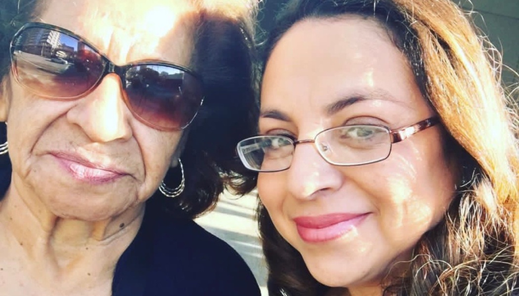 Close-up selfie of an older woman in sunglasses beside a smiling younger woman wearing glasses.