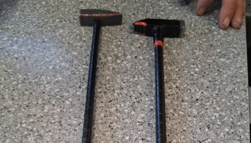 Two custom black metal hammers with red accents resting on a grey speckled surface.