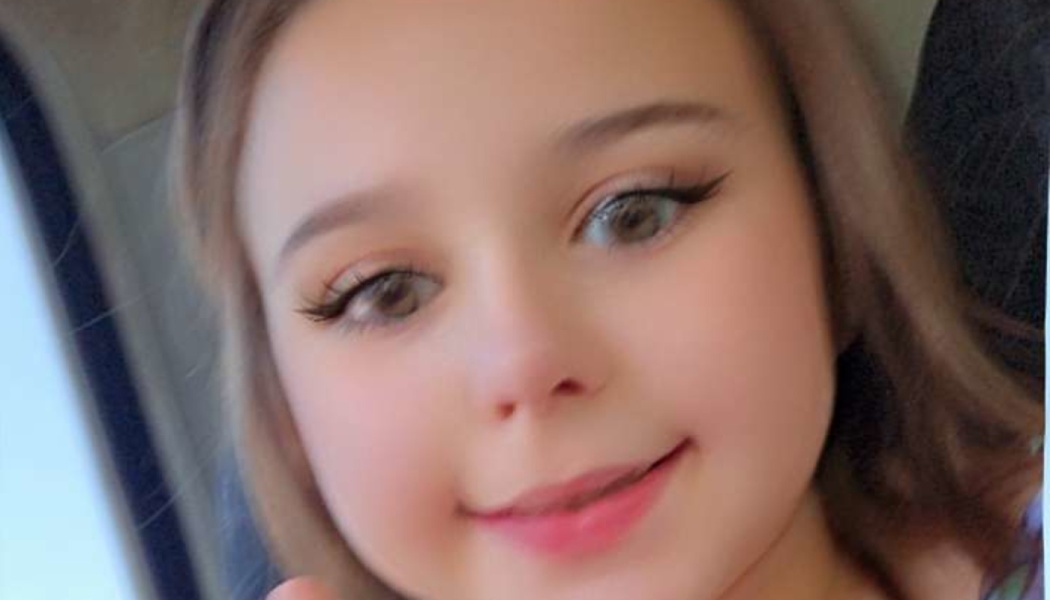 Close-up portrait of a smiling young girl with light brown hair and hazel eyes.