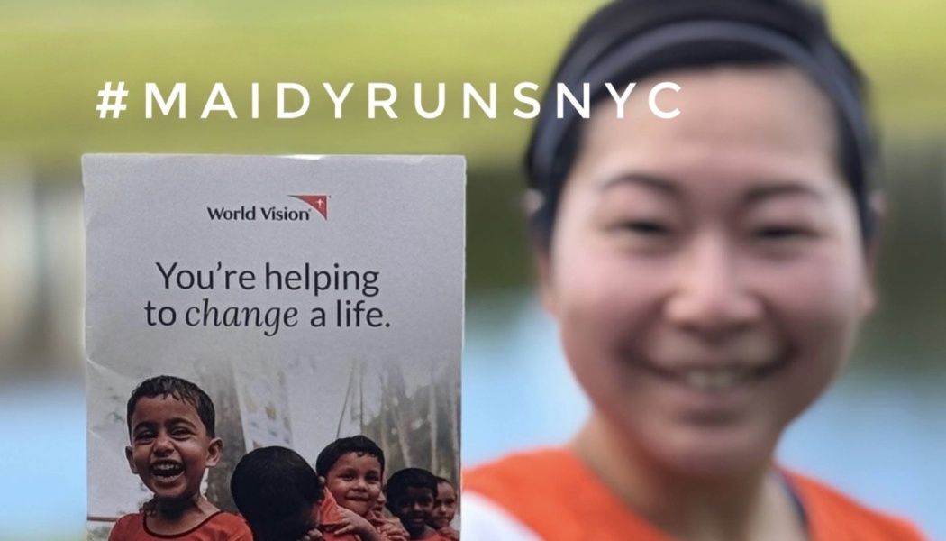 A smiling woman holds a World Vision card reading "You're helping to change a life" with #MAIDYRUNSNYC.