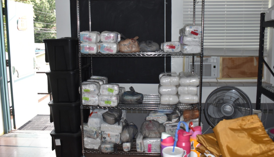 Packages of baby diapers and supplies organized on a wire shelf next to stacked black storage bins.