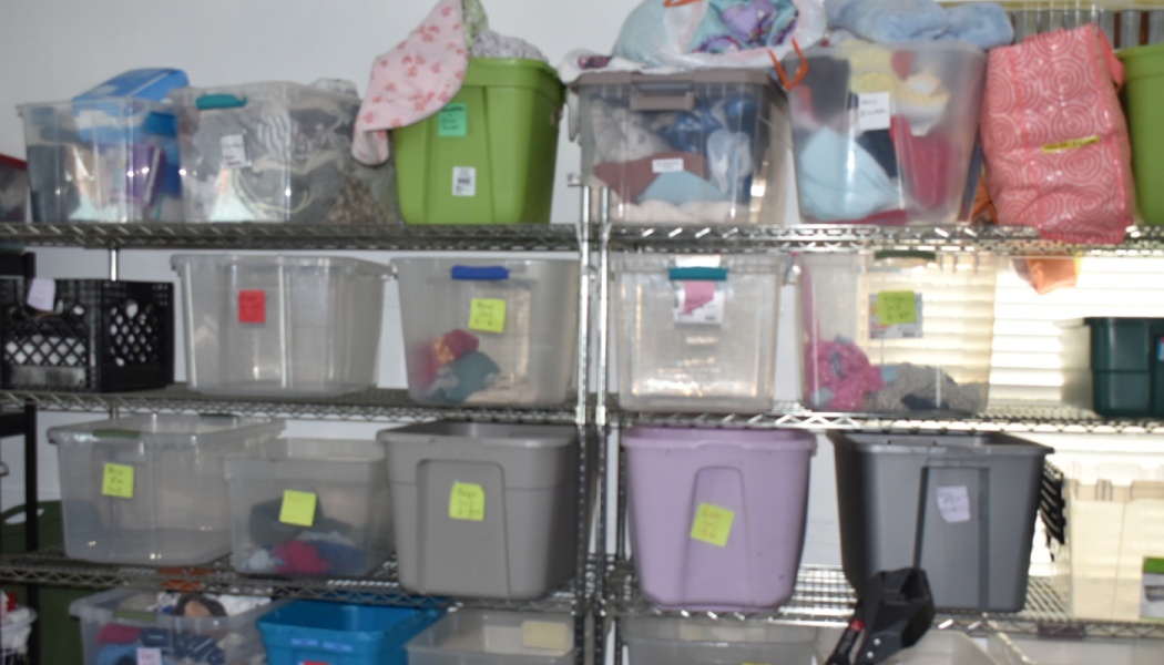 Metal wire shelves packed with labeled plastic storage bins filled with clothes and donation supplies.