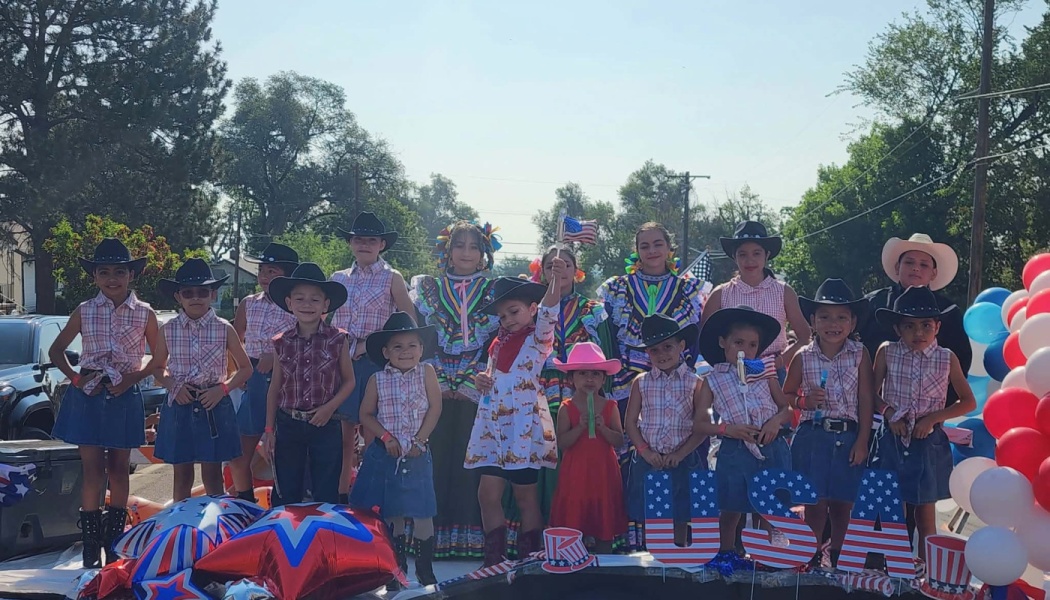 Children in cowboy hats and traditional dresses pose on a patriotic, USA-themed parade float.