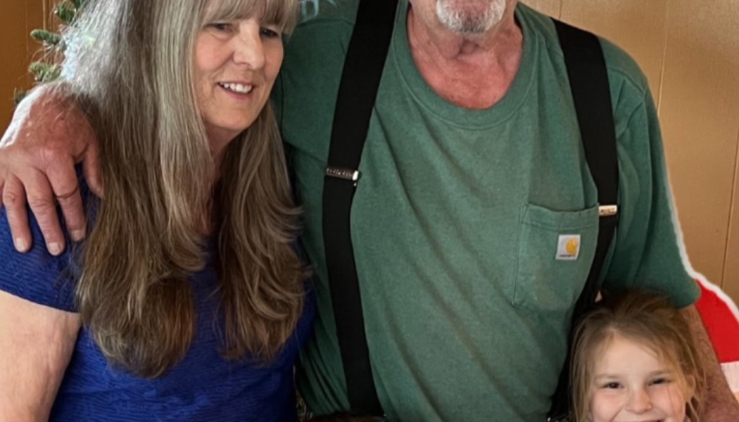 A smiling woman in blue, a man wearing a green shirt with suspenders, and a young girl posing together.