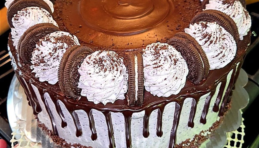 Chocolate drip cake decorated with Oreo cookies, whipped cream swirls, and chocolate crumbs.