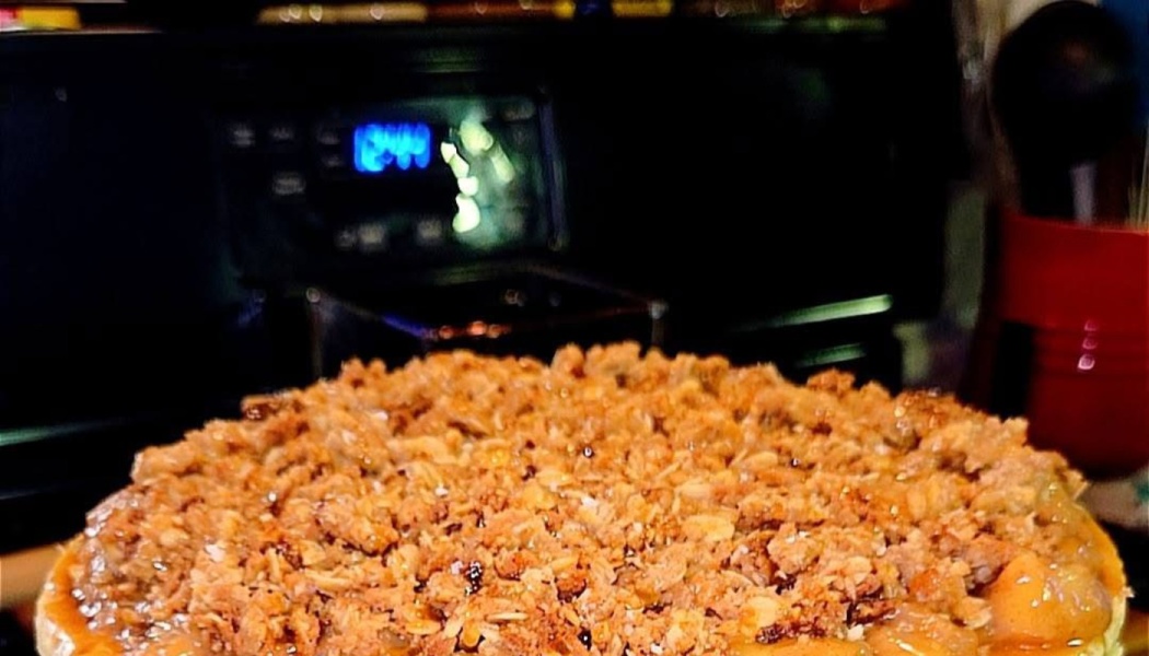 A freshly baked pie topped with a textured golden-brown oat crumble in a dark kitchen.