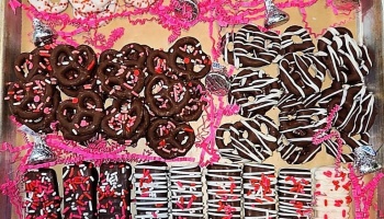 Chocolate-covered pretzels and wafers with Valentine's sprinkles, white drizzle, and pink crinkle paper.