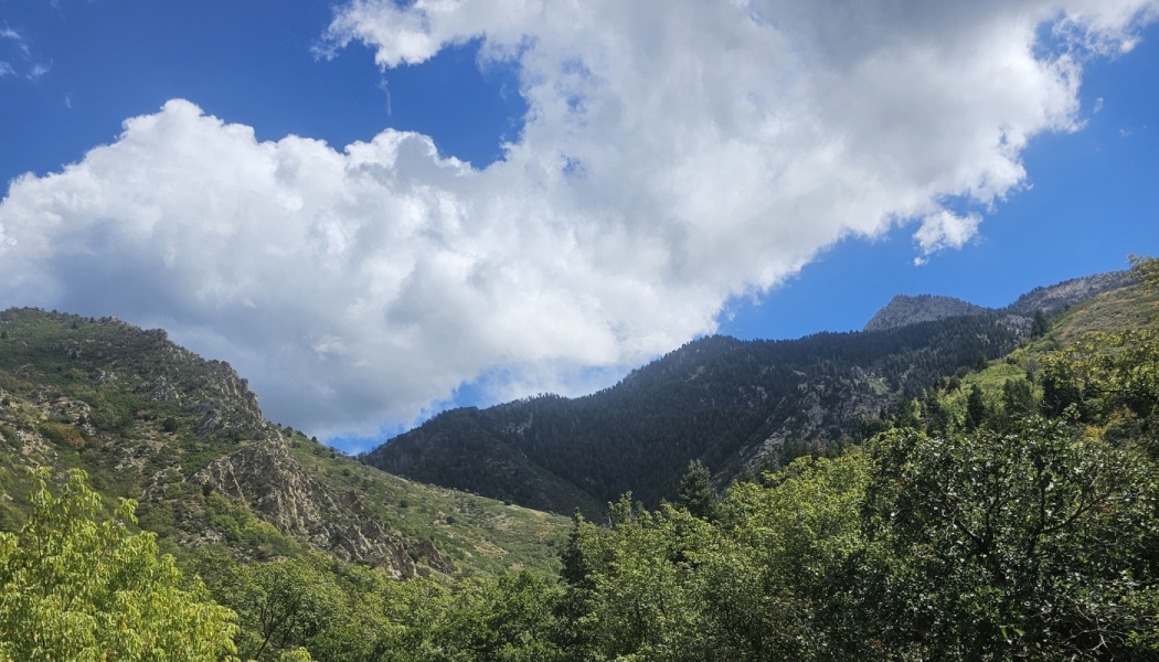 Lush green mountains under a bright blue sky with large, fluffy white clouds.