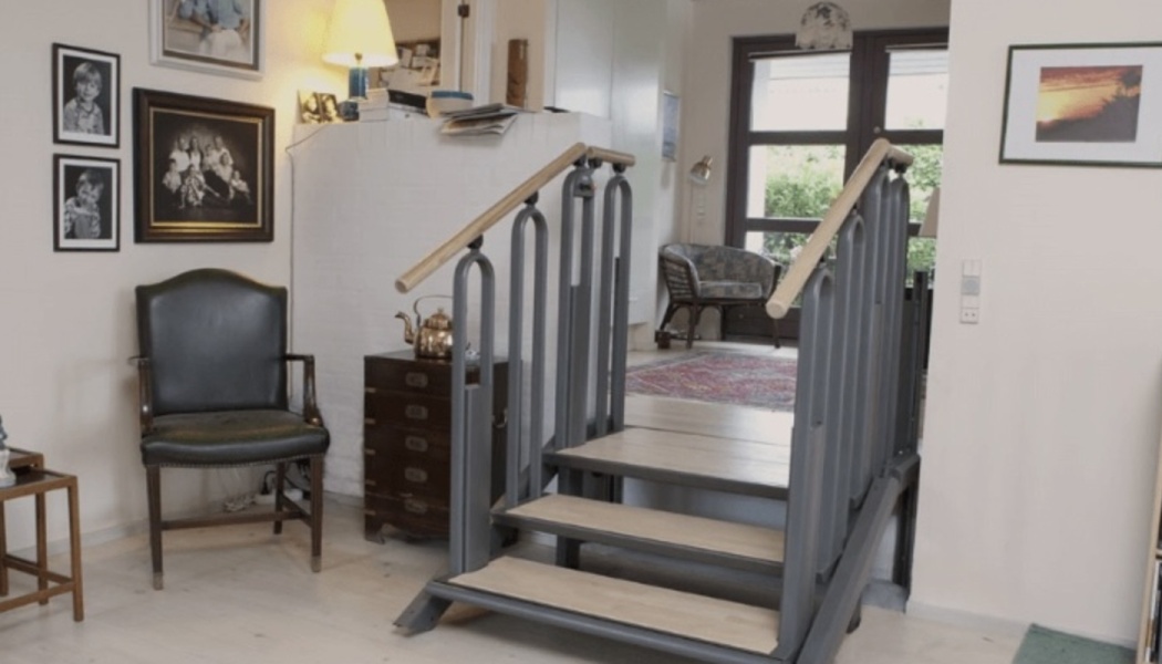 Indoor convertible stair lift with light wood steps and grey handrails in a home living room.