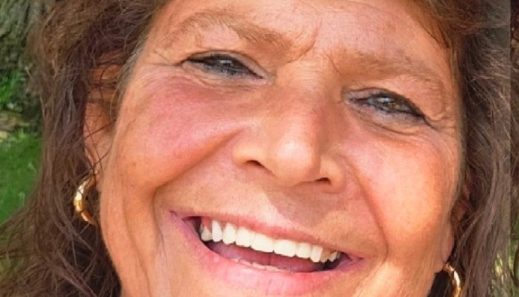 Close-up portrait of a smiling woman with brown hair and gold hoop earrings.
