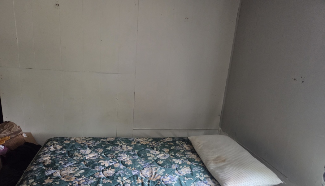 A bare floral-patterned mattress with a single pillow resting against plain, off-white walls in a room corner.