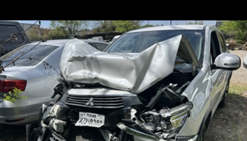 A white Mitsubishi SUV with severe front-end crash damage and a heavily crumpled hood.