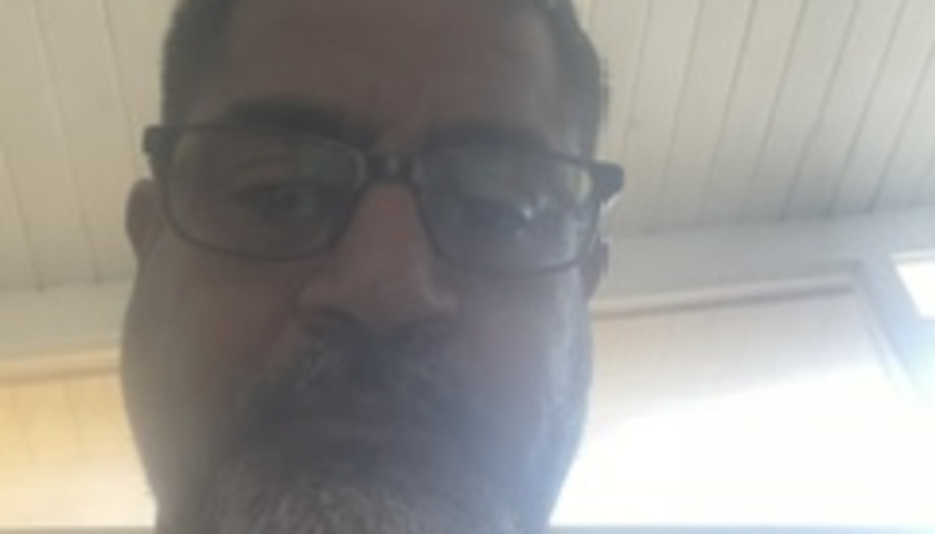 Close-up selfie of a man with glasses and a graying beard looking down at the camera.