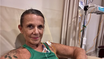 A smiling woman in a green tank top receiving IV medical treatment while seated in a clinic chair.
