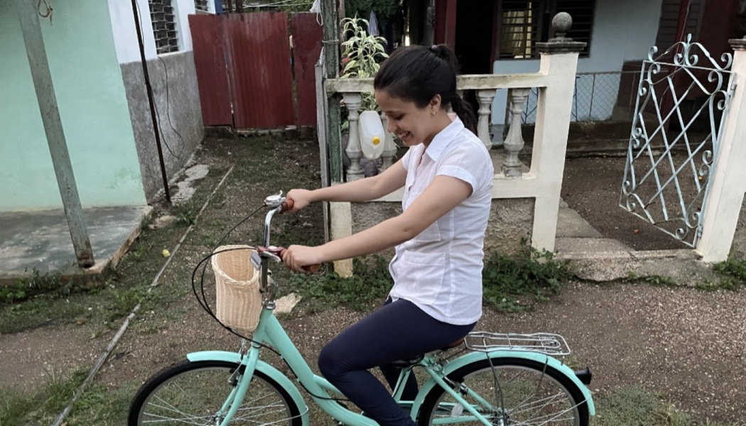 A smiling young woman in a white shirt riding a mint green bicycle with a wicker basket.