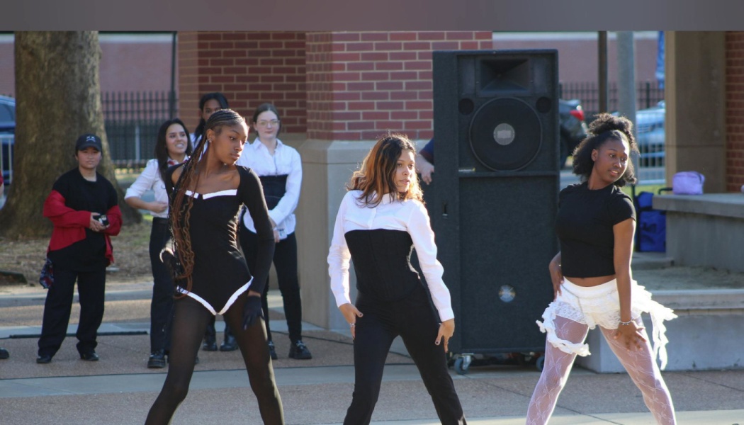 Three dancers perform a routine outdoors in black and white outfits in front of a large speaker.