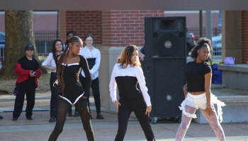 Three dancers perform a routine outdoors in black and white outfits in front of a large speaker.