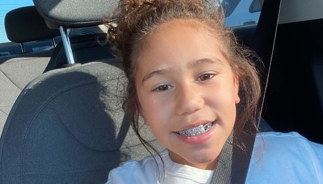 Young girl with curly hair and braces smiling warmly while sitting in a car.