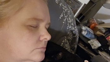 Close-up of a fair-skinned person with blonde hair sleeping peacefully on a patterned grey pillow.