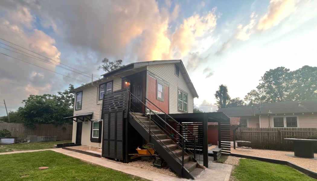 Two-story renovated house with a black exterior staircase and patio area beneath a dramatic sunset sky.